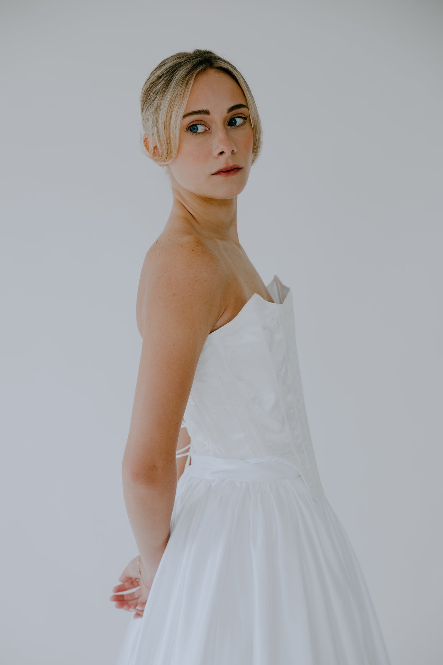 Woman wearing a white wedding corset and skirt set against a plain background