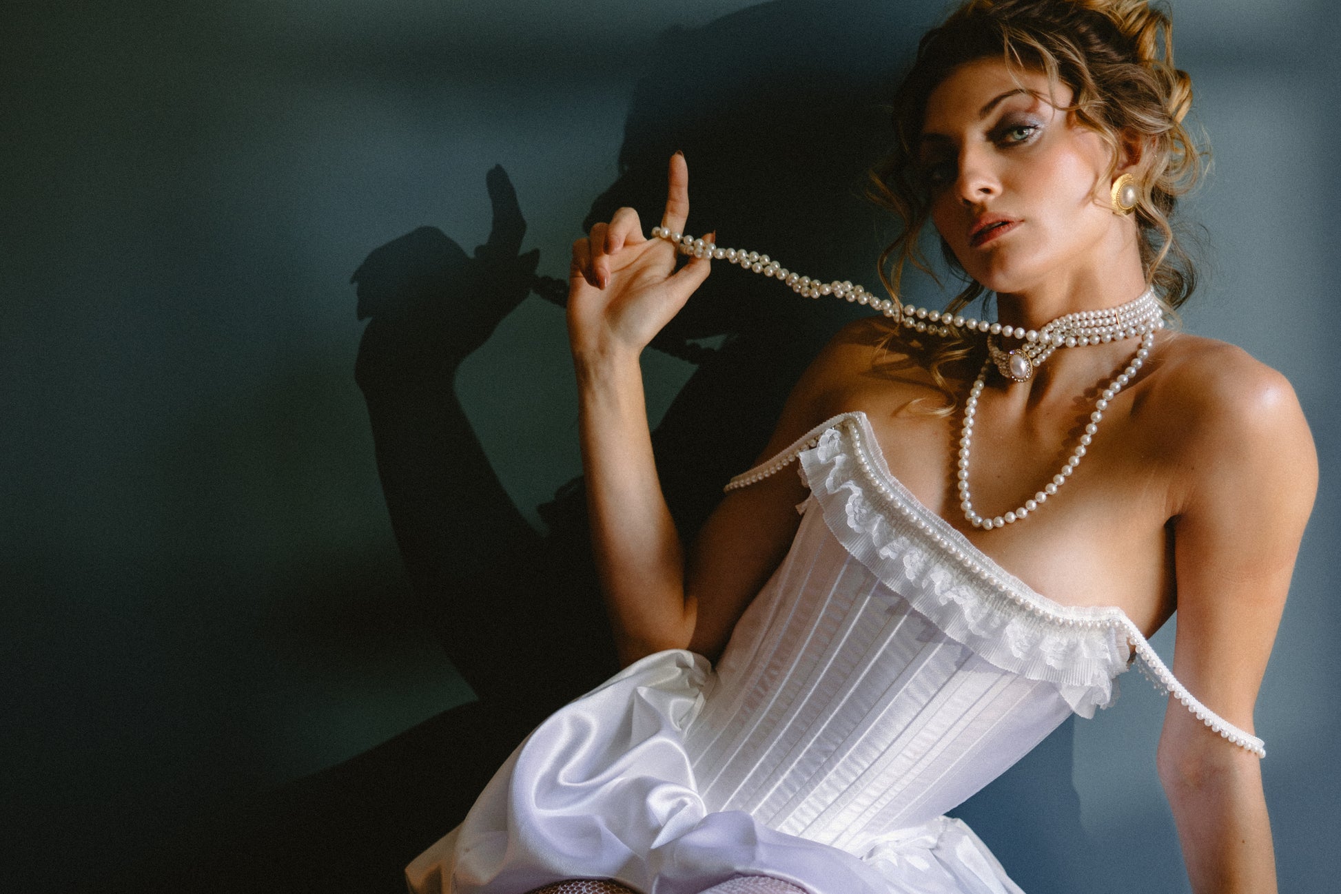 Bride in a white corset holding a pearl necklace against a dark background