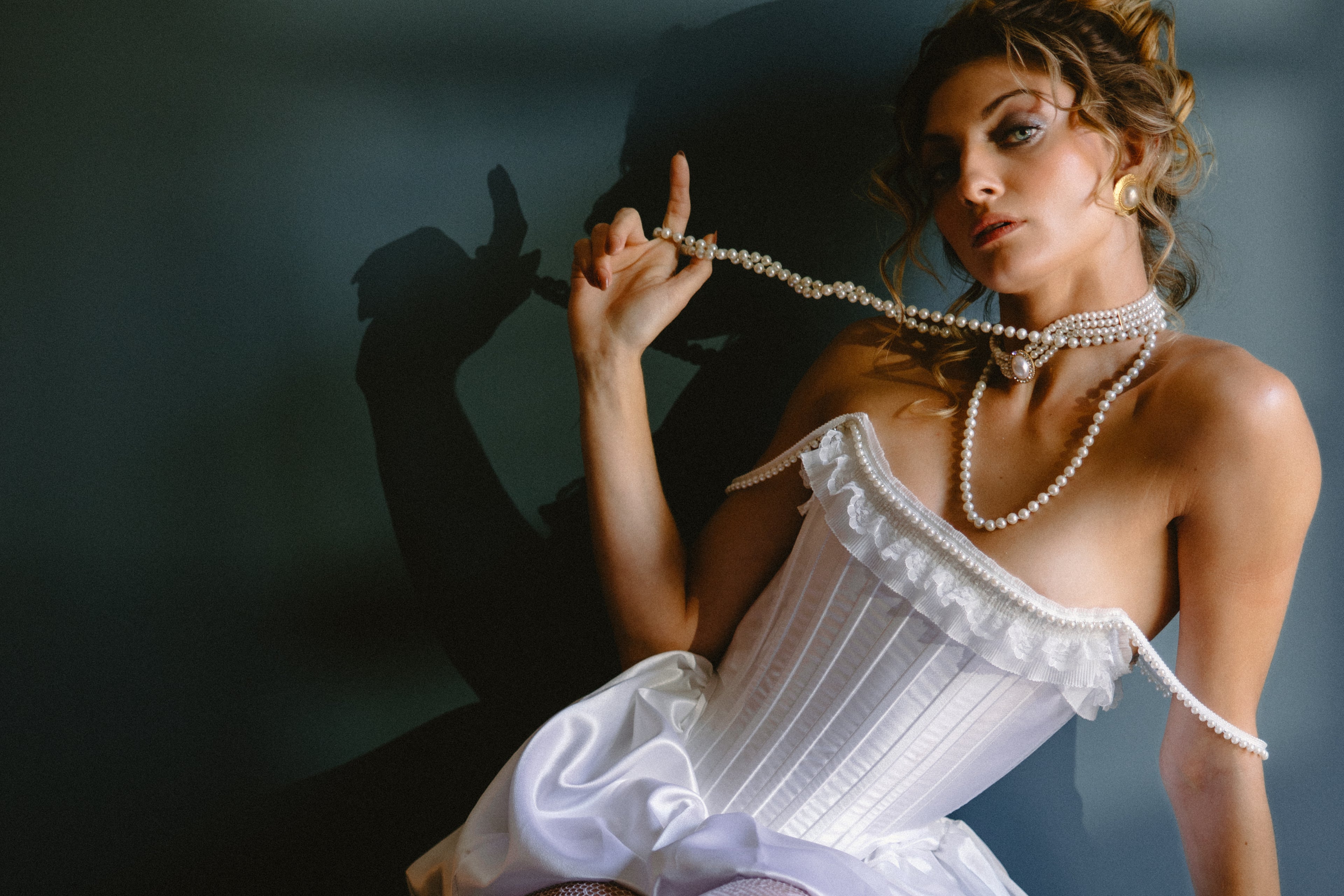 Bride in a white corset holding a pearl necklace against a dark background