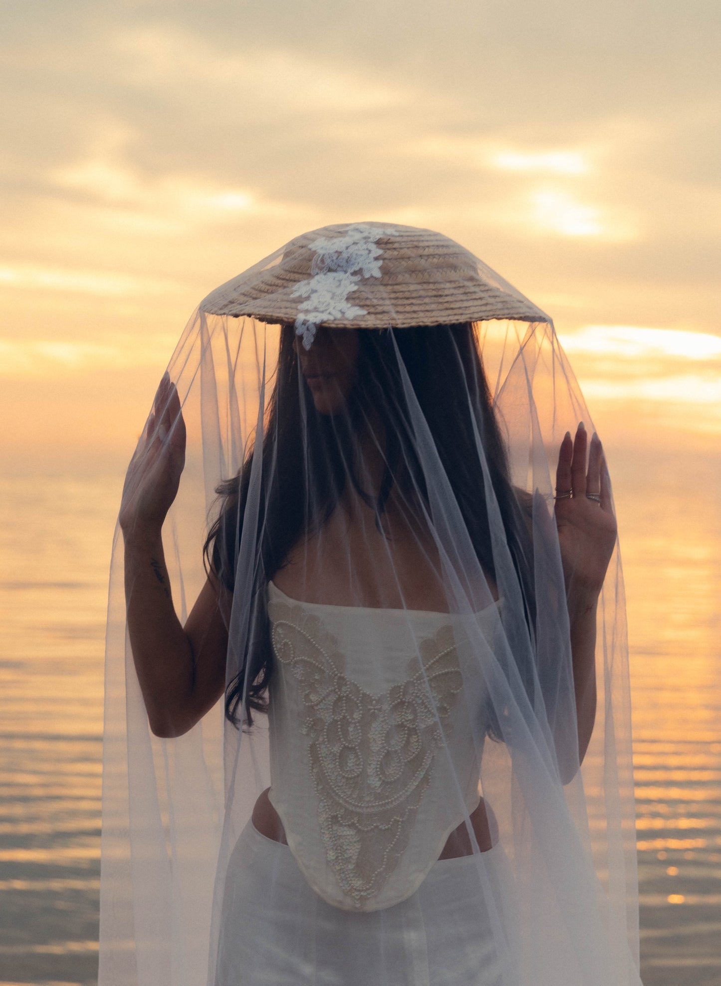 Bride in a wedding corset with a veil and hat against a sunset background