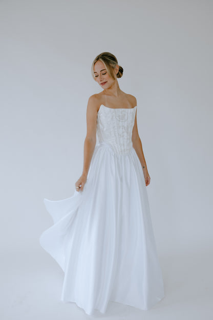 Woman wearing a white bridal wedding dress against a plain background