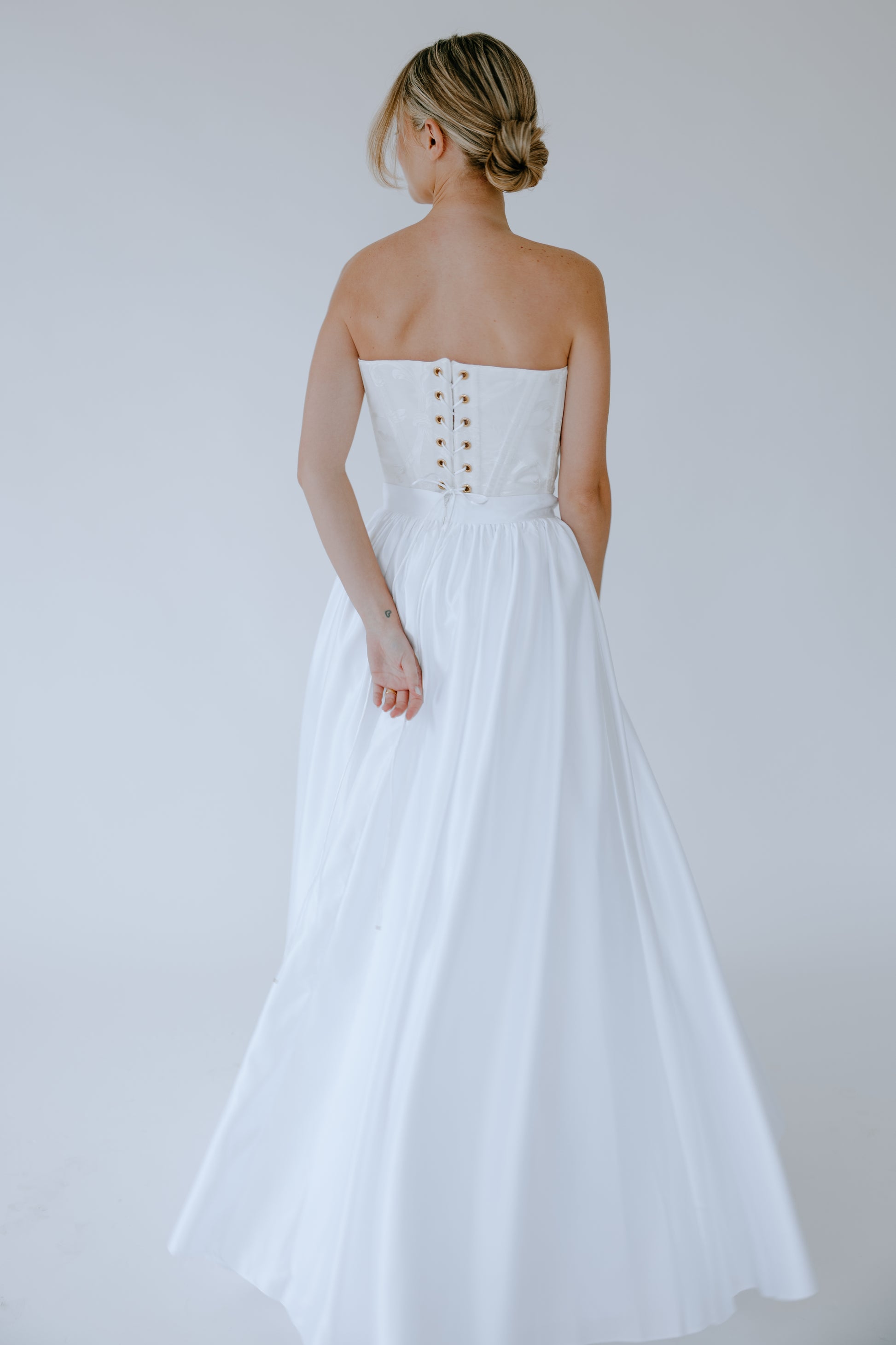 Woman wearing a white wedding dress with a lace up back on a plain background