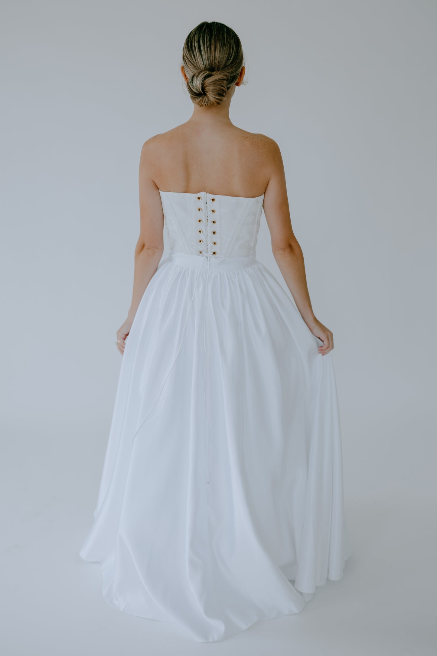 Woman wearing a white corset and skirt set with a lace up back on a plain background