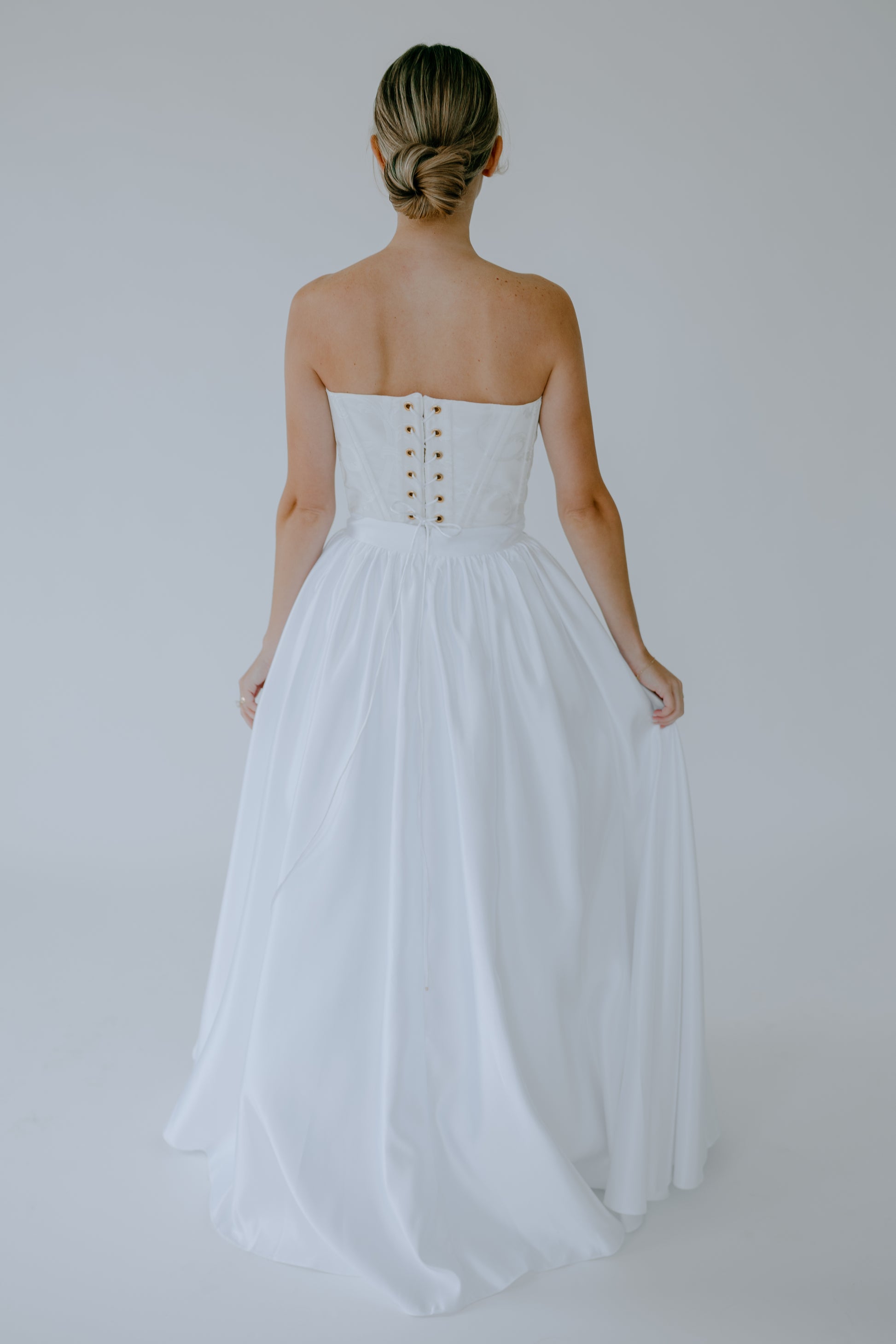 Woman wearing a white corset and skirt set with a lace up back on a plain background