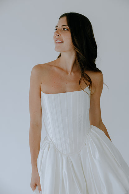 Woman wearing a bridal corset and skirt set against a plain background