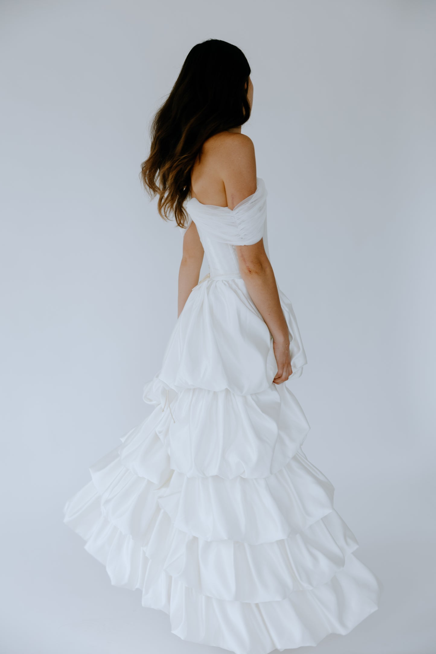Woman wearing a white off-shoulder wedding dress against a plain background