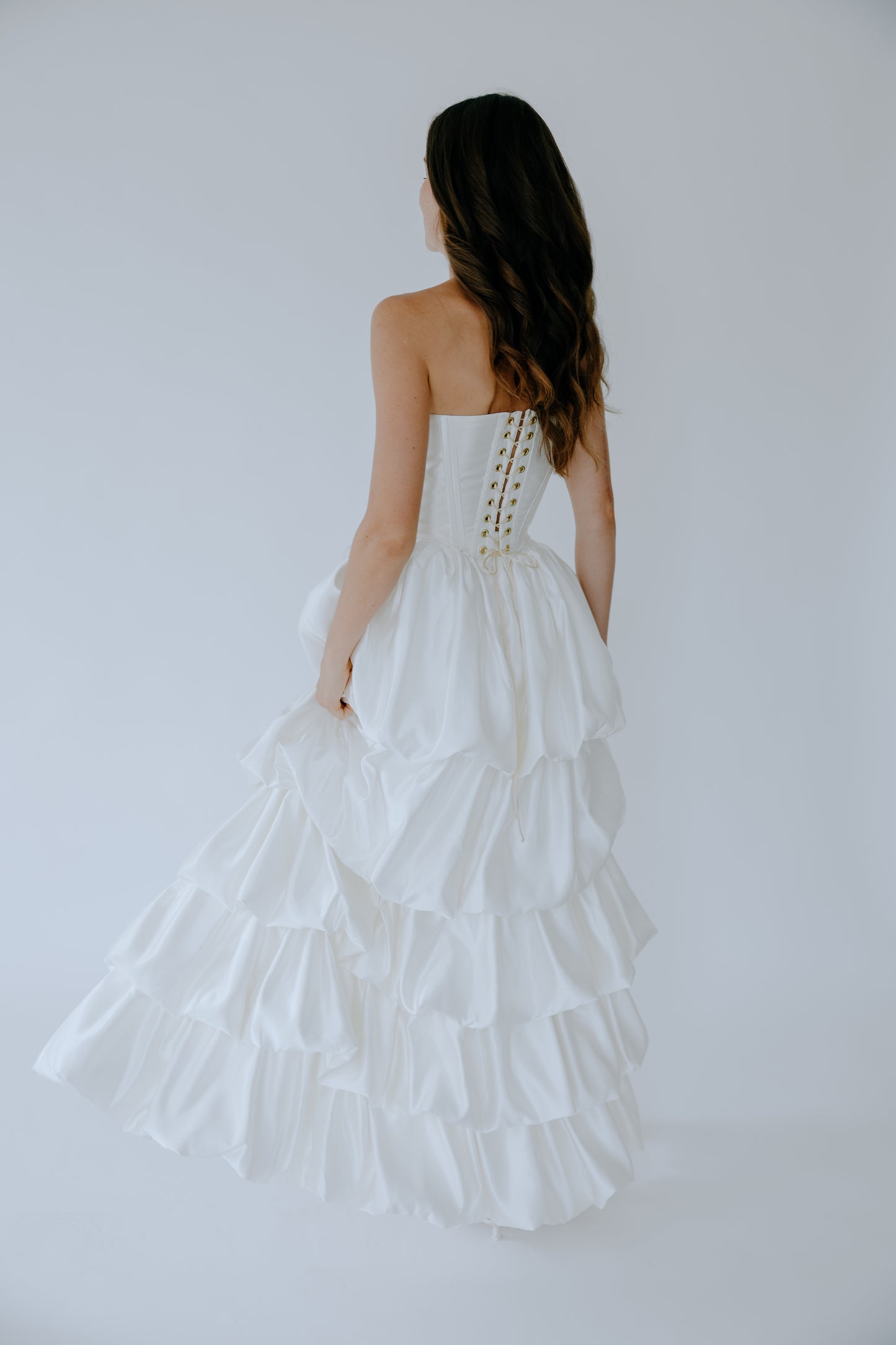 Woman wearing a white bridal corset with a ruffled satin skirt on a plain background