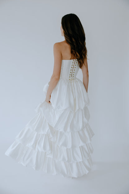 Woman wearing a white bridal corset with a ruffled satin skirt on a plain background