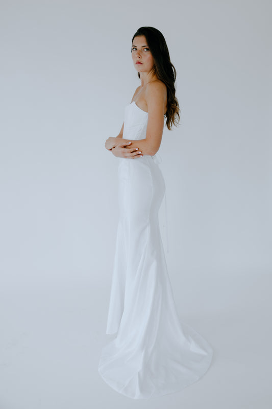 Woman in a white wedding gown standing against a plain background